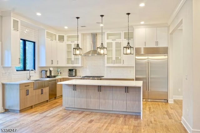 kitchen featuring appliances with stainless steel finishes, decorative light fixtures, white cabinets, a large island, and wall chimney range hood