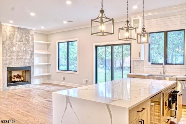 kitchen featuring pendant lighting, sink, light stone counters, a kitchen island, and built in shelves