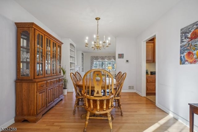 dining space with light wood-type flooring, built in features, and a notable chandelier