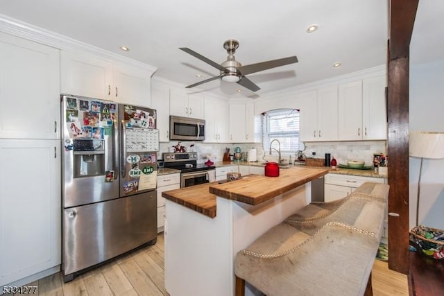 kitchen with butcher block countertops, stainless steel appliances, a center island, white cabinets, and a kitchen bar