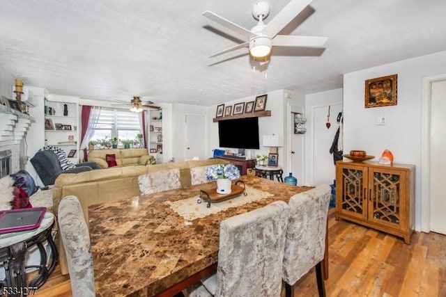 dining space featuring a brick fireplace, ceiling fan, and light hardwood / wood-style flooring