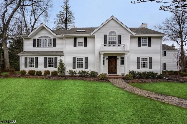 colonial inspired home featuring a balcony and a front lawn