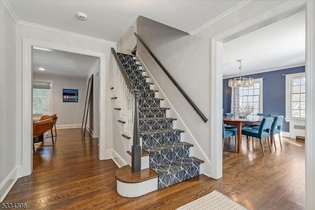 stairs with crown molding, wood-type flooring, a chandelier, and radiator heating unit