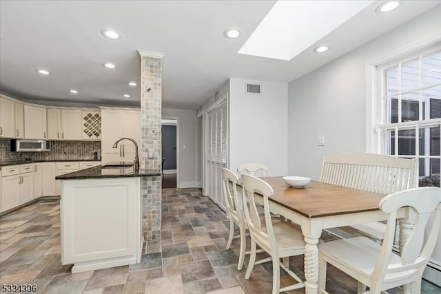 kitchen with sink, a kitchen island with sink, a skylight, decorative backsplash, and cream cabinetry