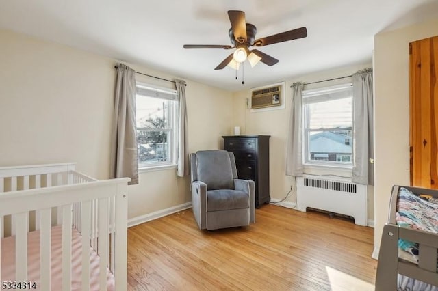 bedroom with radiator, a wall mounted AC, ceiling fan, a crib, and light hardwood / wood-style flooring