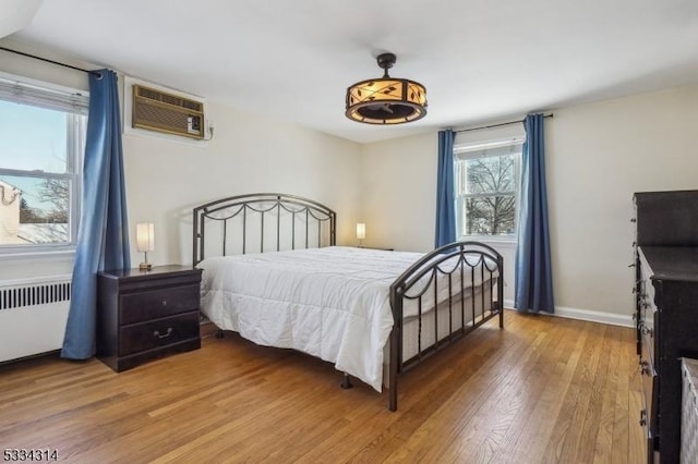 bedroom with hardwood / wood-style floors, an AC wall unit, and radiator heating unit