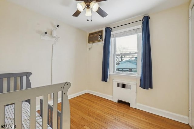 bedroom with a wall mounted AC, radiator heating unit, ceiling fan, and light hardwood / wood-style floors