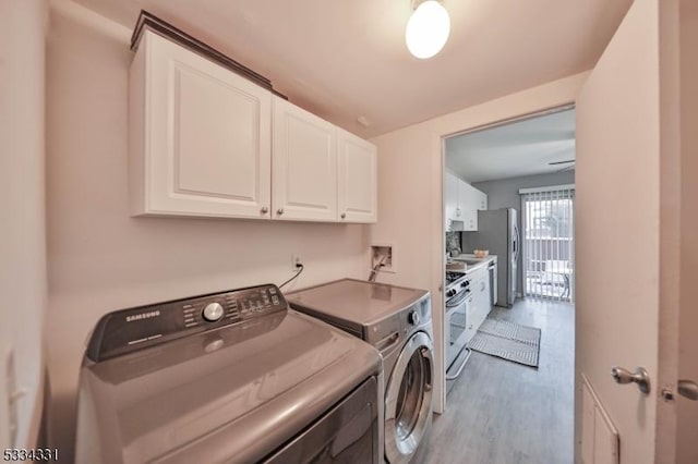 clothes washing area featuring cabinets, washing machine and dryer, and light hardwood / wood-style flooring