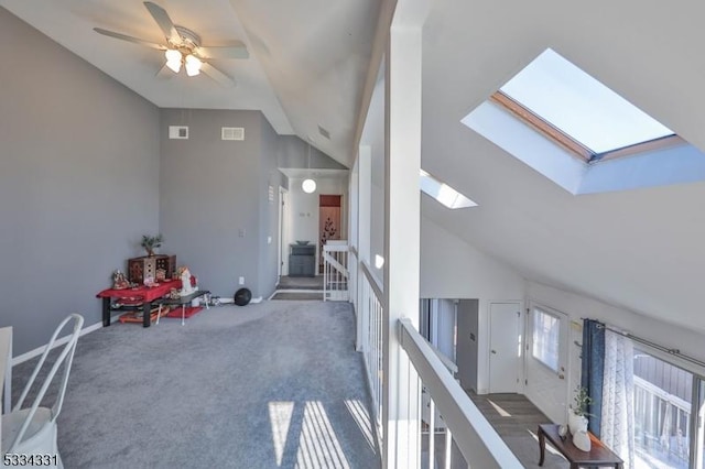 interior space featuring dark colored carpet, lofted ceiling with skylight, and ceiling fan