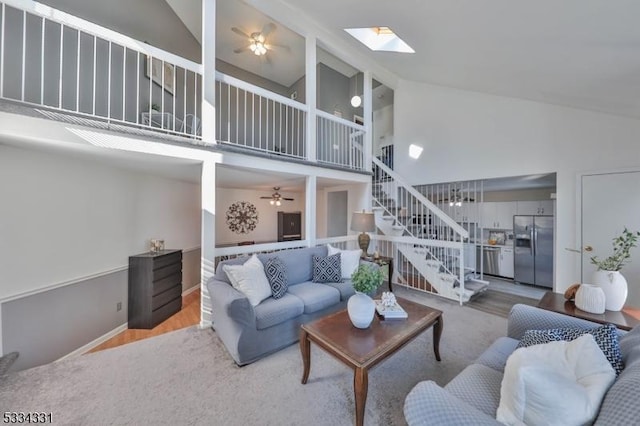 living room with hardwood / wood-style flooring, ceiling fan, a skylight, and high vaulted ceiling