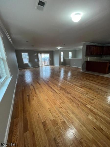 unfurnished living room with hardwood / wood-style flooring and crown molding