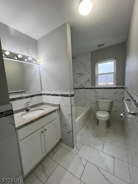 bathroom featuring vanity, tile walls, and toilet