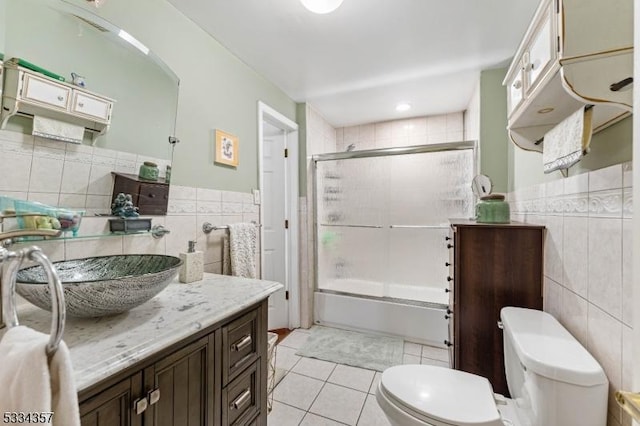 full bathroom with shower / bath combination with glass door, tile walls, vanity, tile patterned floors, and toilet