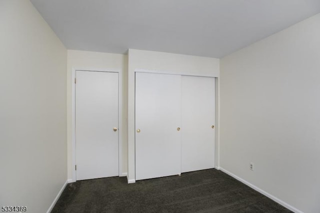 unfurnished bedroom with dark carpet and a closet