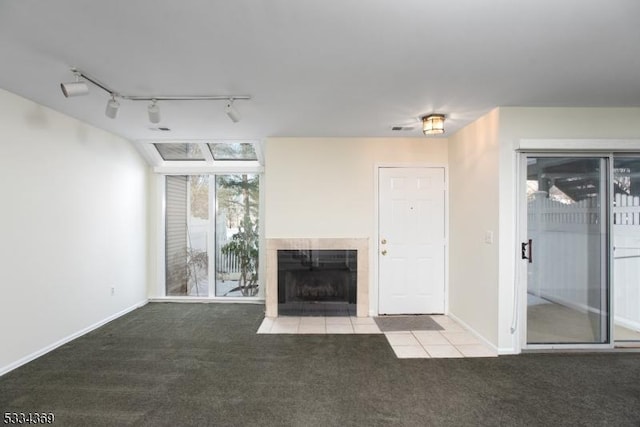 unfurnished living room featuring carpet floors, a tile fireplace, and track lighting