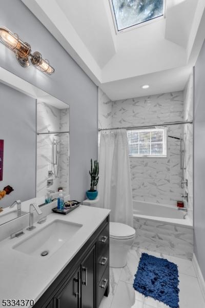 full bathroom featuring vanity, a skylight, shower / bath combination with curtain, and toilet