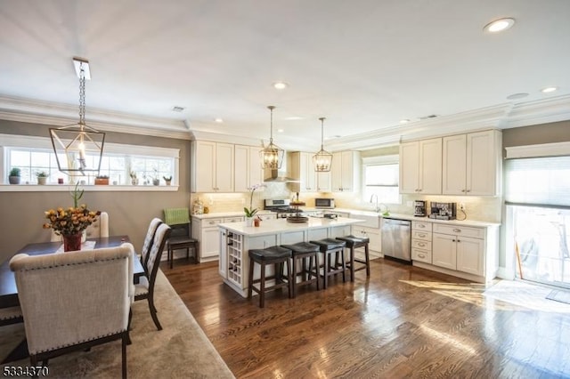 kitchen featuring wall chimney range hood, appliances with stainless steel finishes, a kitchen breakfast bar, a center island, and decorative light fixtures