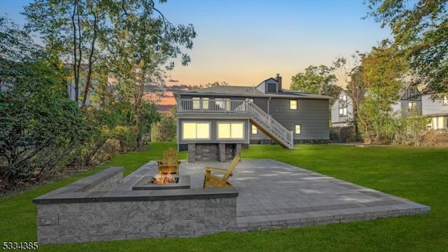 back house at dusk featuring a yard, a patio area, a balcony, and an outdoor fire pit