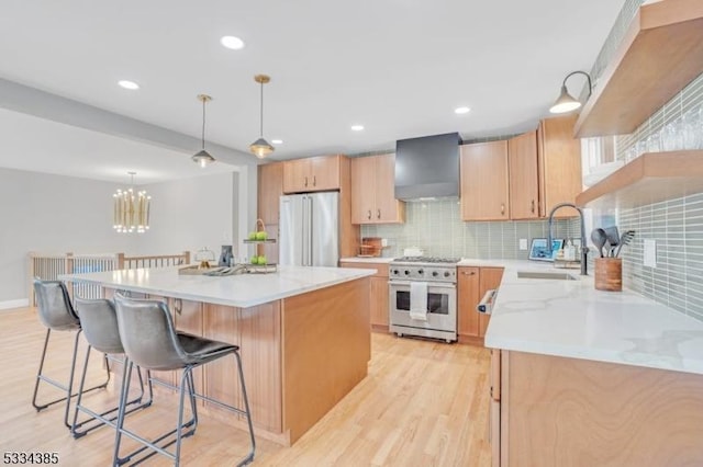 kitchen with a kitchen island, appliances with stainless steel finishes, decorative light fixtures, sink, and wall chimney range hood