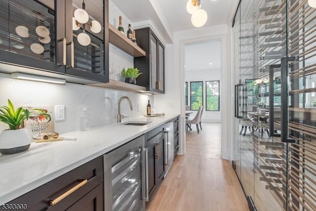 bar with sink, beverage cooler, decorative backsplash, light stone counters, and light wood-type flooring