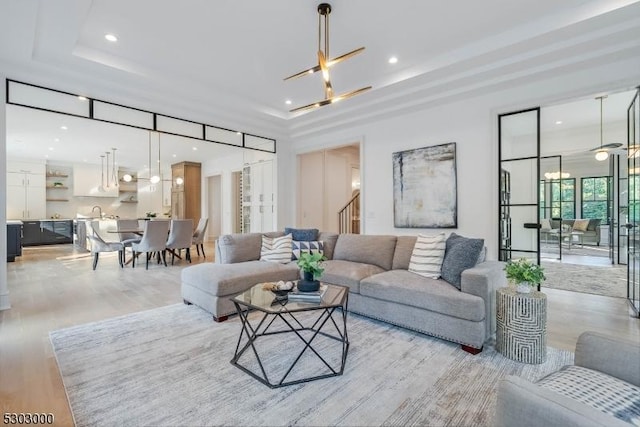 living room featuring a raised ceiling, sink, and light wood-type flooring