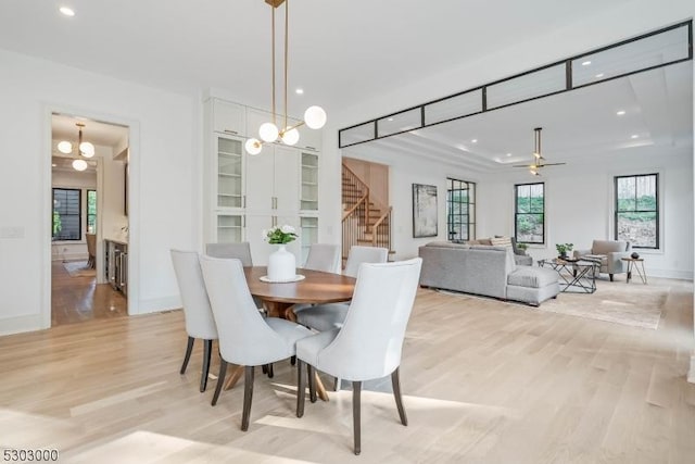 dining area with ceiling fan with notable chandelier and light hardwood / wood-style floors