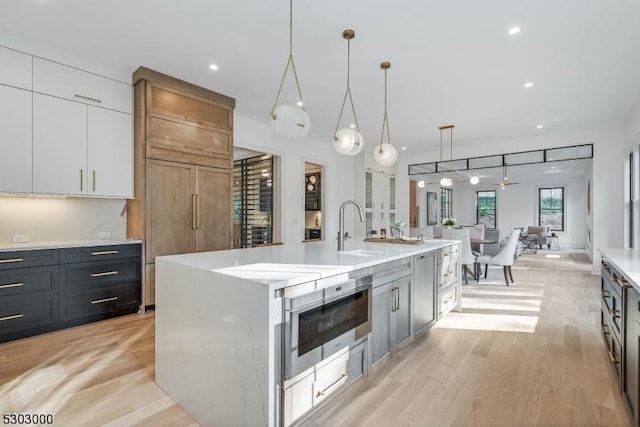 kitchen featuring sink, white cabinetry, light wood-type flooring, an island with sink, and pendant lighting