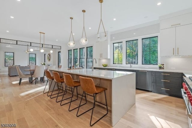 kitchen featuring pendant lighting, a breakfast bar, white cabinetry, stainless steel dishwasher, and a large island with sink