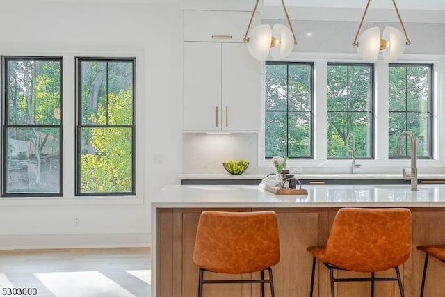 kitchen featuring pendant lighting, sink, light hardwood / wood-style flooring, white cabinetry, and a kitchen bar