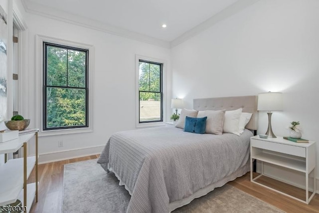 bedroom featuring multiple windows, ornamental molding, and light hardwood / wood-style flooring