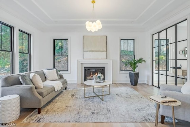 living room with an inviting chandelier, hardwood / wood-style floors, a tray ceiling, and crown molding