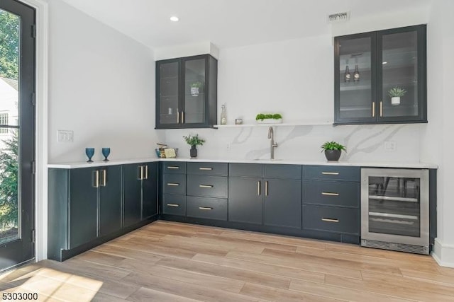 bar featuring decorative backsplash, sink, wine cooler, and light hardwood / wood-style flooring