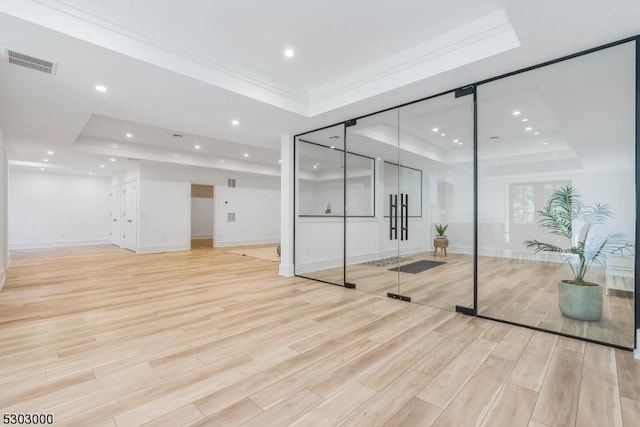 interior space with crown molding, a raised ceiling, and light wood-type flooring