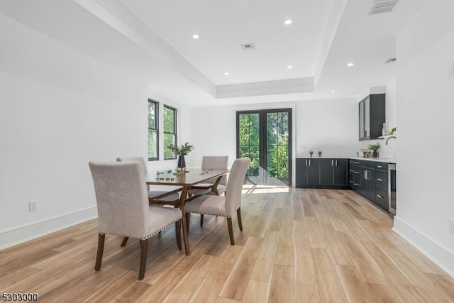 dining room with french doors, crown molding, a raised ceiling, and light wood-type flooring