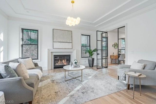 living room with plenty of natural light, light hardwood / wood-style floors, a raised ceiling, and a chandelier