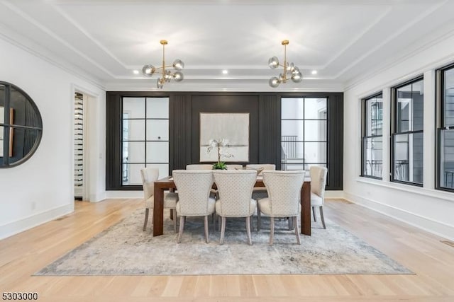 dining space with crown molding, a notable chandelier, light wood-type flooring, and a tray ceiling