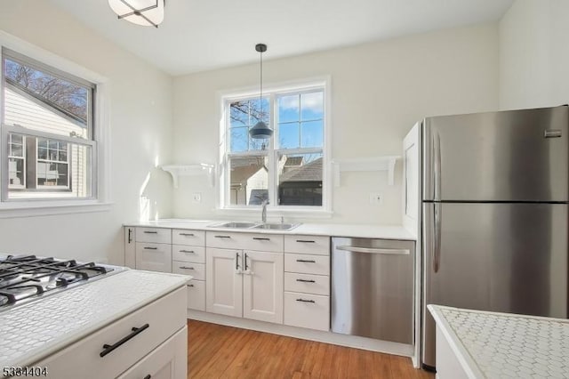 kitchen with sink, light hardwood / wood-style flooring, appliances with stainless steel finishes, hanging light fixtures, and white cabinets