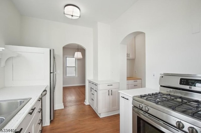 kitchen featuring appliances with stainless steel finishes, pendant lighting, sink, white cabinets, and light hardwood / wood-style floors