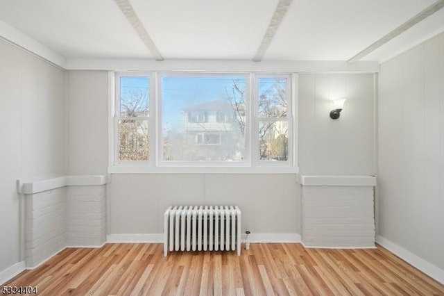 unfurnished room featuring beamed ceiling, radiator, a wealth of natural light, and light wood-type flooring