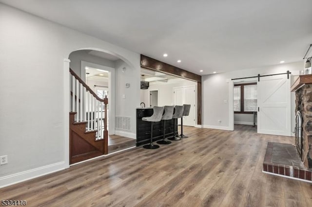 living room with wood-type flooring, a barn door, and indoor bar