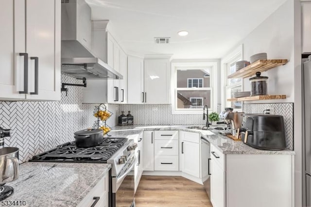 kitchen with stainless steel gas stove, sink, white cabinets, light stone counters, and wall chimney range hood