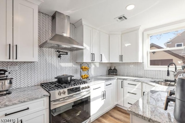 kitchen with tasteful backsplash, white cabinets, stainless steel range with gas cooktop, and wall chimney exhaust hood