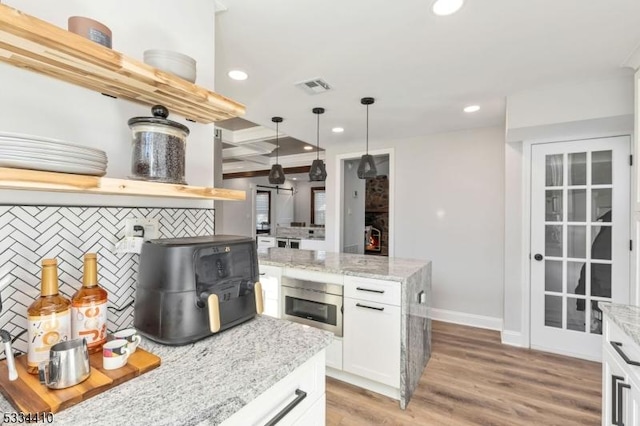 kitchen featuring pendant lighting, tasteful backsplash, beamed ceiling, light stone countertops, and white cabinets