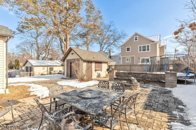 snow covered patio with a trampoline, an outdoor fire pit, and a storage unit