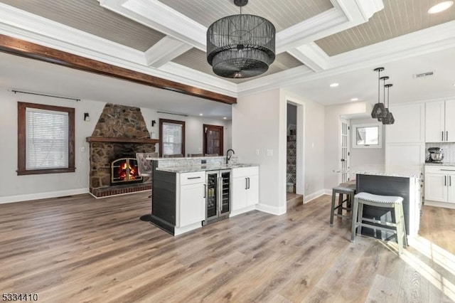 kitchen with white cabinetry, decorative light fixtures, light stone countertops, and beverage cooler