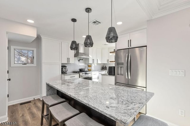 kitchen with appliances with stainless steel finishes, white cabinetry, hanging light fixtures, light stone countertops, and wall chimney exhaust hood