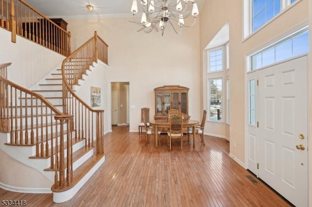 foyer entrance featuring ornamental molding, wood-type flooring, a high ceiling, and a notable chandelier