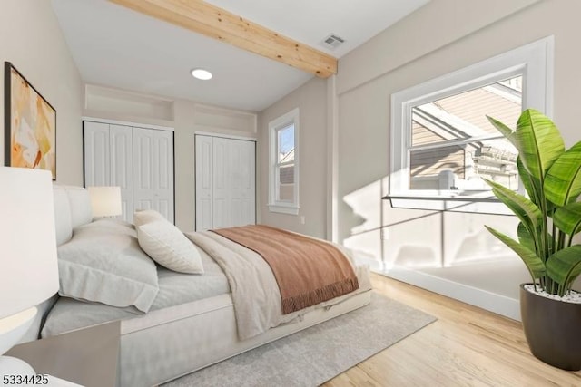 bedroom with beamed ceiling, multiple closets, and light wood-type flooring