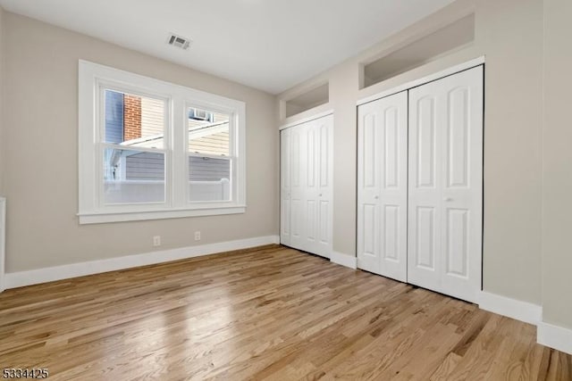 unfurnished bedroom with two closets and light wood-type flooring