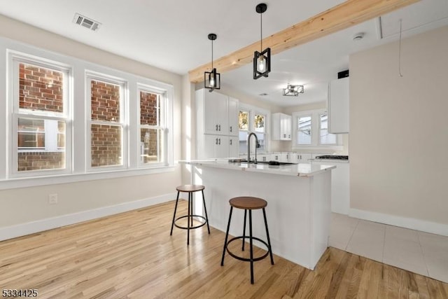 kitchen with white cabinetry, a center island, decorative light fixtures, beamed ceiling, and light wood-type flooring